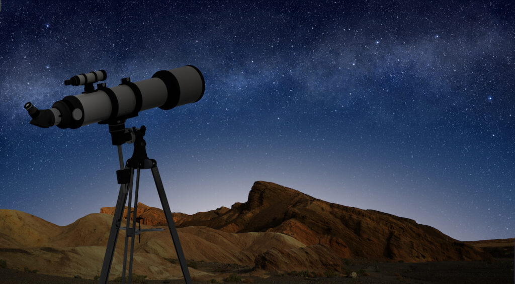 Refractive telescope on a tripod pointing at starry night sky